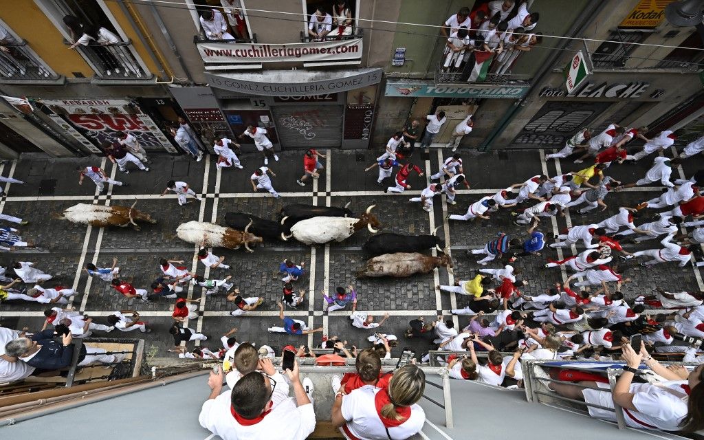 Participants run ahead of bulls during the first "encierro" (bull-run) of the San Fermin festival in Pamplona, northern Spain, on July 7, 2025. Thousands of people every year attend the week-long festival and its famous 'encierros': six bulls are released at 8:00 a.m. evey day to run from their corral to the bullring through the narrow streets of the old town over an 850 meters (yard) course while runners ahead of them try to stay close to the bulls without falling over or being gored. (Photo by Ander GILLENEA / AFP)