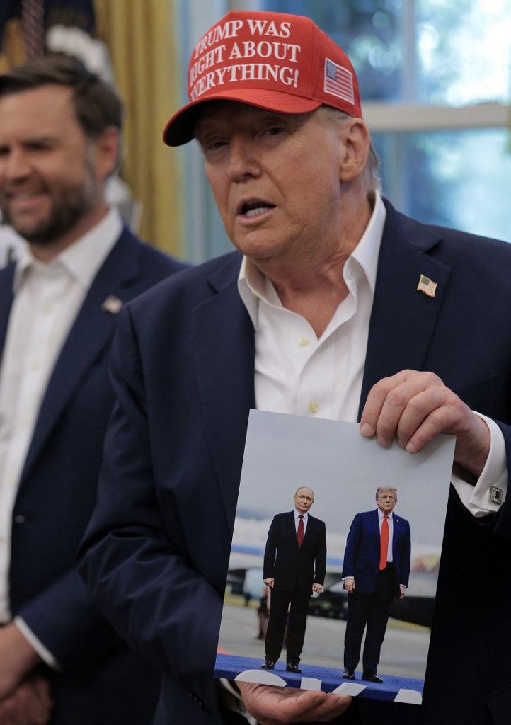 Donald Trump amerikai elnök egy fényképet tart a kezében, amelyen ő maga és Vlagyimir Putyin látható
