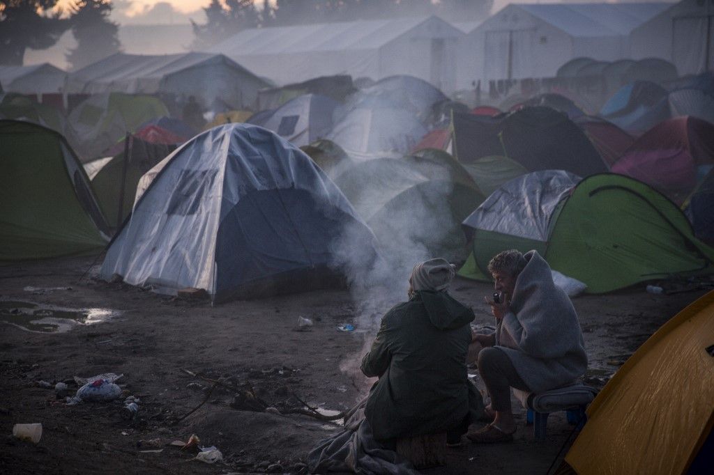 IDOMENI, GREECE-- People warmed themselves by a fire after a rain storm the previous night soaked through tents and made for miserable conditons. More than 13,000 people, mainly Syrian and Iraqi refugees, are trapped at the Idomeni border camp on the Greek side of the Greek/Macedonian border on March 8, 2015.  (Photo by Jodi Hilton/NurPhoto) (Photo by JODI HILTON / NurPhoto via AFP)