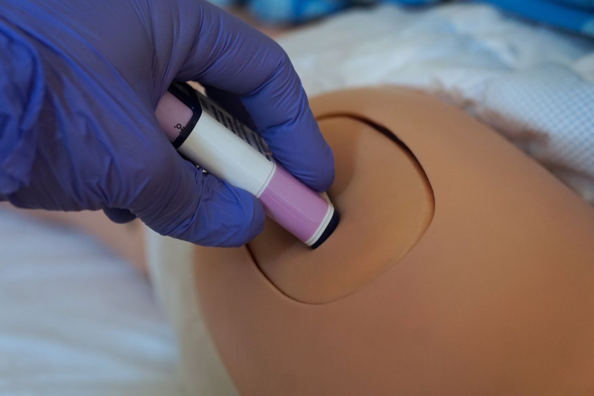 The use of an epinephrine auto-injector training device on a medical mannequin during a simulation exercise, demonstrating intramuscular epipen application for anaphylaxis and allergy first aid.