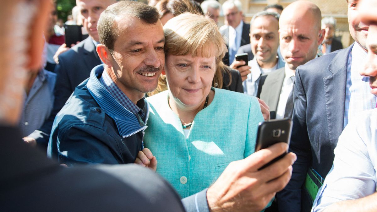 (FILES) In this file photo taken on September 10, 2015 an asylum seeker (C, L) takes a selfie picture with German Chancellor Angela Merkel (C, R) following Merkel's visit at a branch of the Federal Office for Migration and Refugees and a camp for asylum-seekers in Berlin. "We can do this," Angela Merkel famously declared on August 31, 2015 as columns of desperate people walked through the Balkans towards Germany. Civil wars were raging in Syria and Afghanistan, driving the largest wave of refugees since World War II, with the Mediterranean Sea becoming a mass grave. (Photo by BERND VON JUTRCZENKA / DPA / AFP)