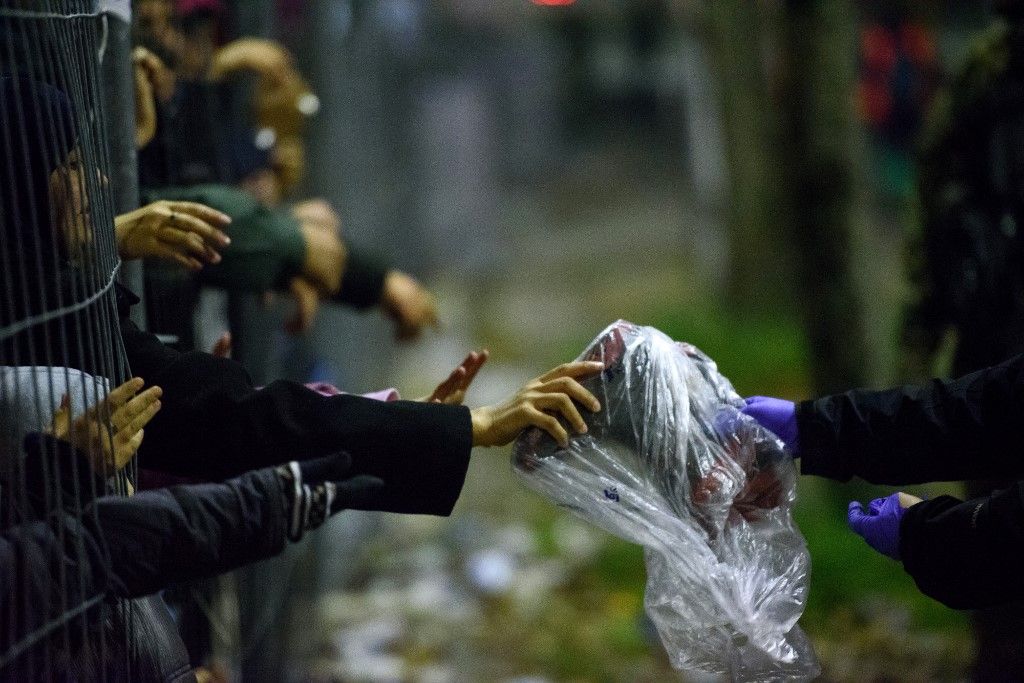 Migrants and refugees reach through a fence for clothes and food from volunteers as they wait to cross the Slovenian-Austrian border in Sentilj on October 31, 2015. AFP PHOTO / JURE MAKOVEC (Photo by Jure Makovec / AFP)
