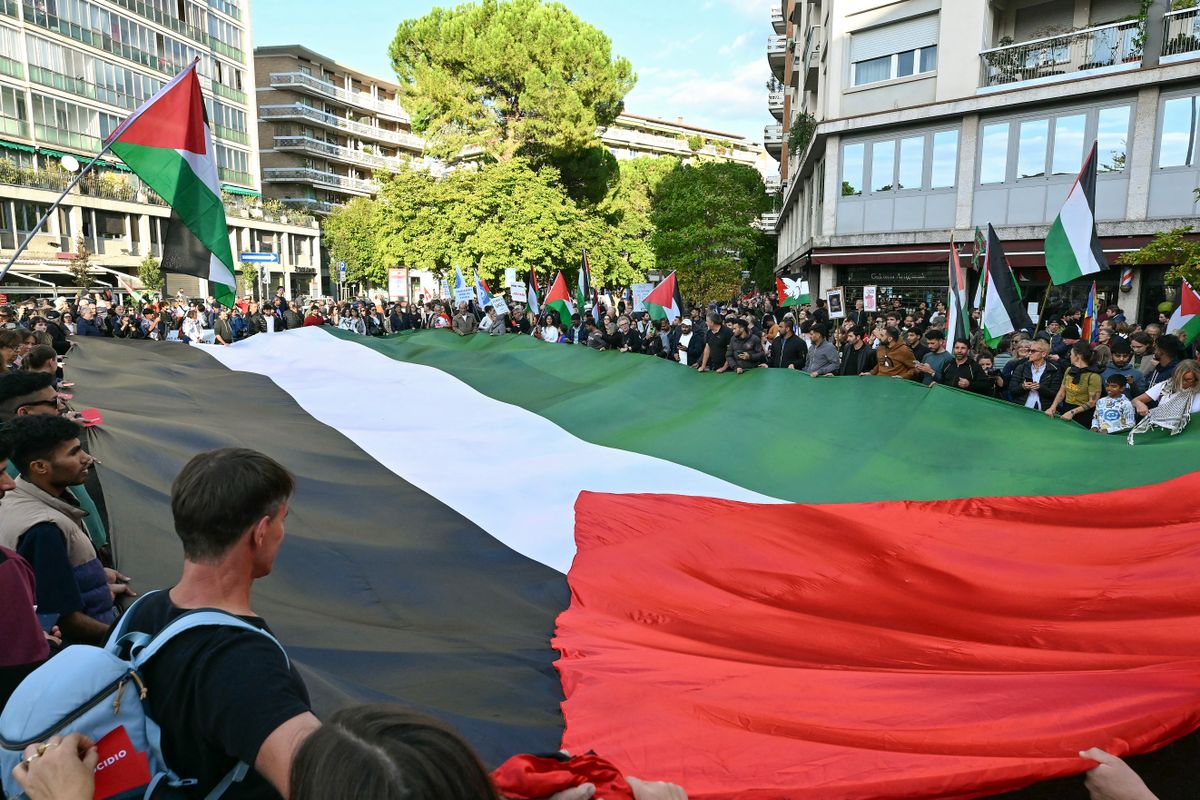 Pro-Palestinian protesters hold the edge of a large Palestinian flag as they gather in solidarity with Palestine, on the eve of the match between Italy and Israel for the FIFA World Cup 2026 qualifiers, in Udine northeastern Italy, on October 14, 2025. The Gaza ceasefire deal signed on October 13, 2025 and a hostage and prisoner exchange between Israel and Hamas has done nothing to dampen the resolve of around 10,000 protestors who march through Udine in anger at the hosting of a match they feel should not be played. (Photo by Stefano RELLANDINI / AFP)