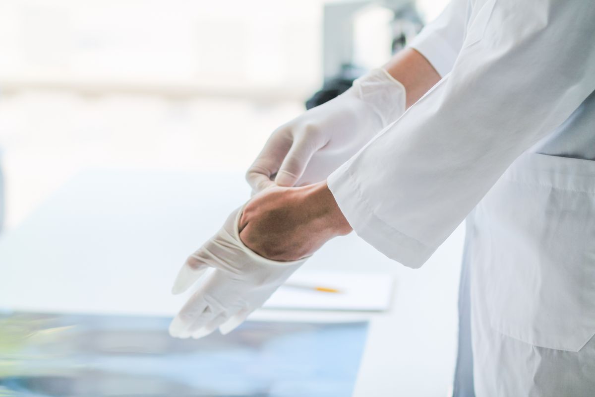 doctor is wearing white rubber gloves prevent direct contact with patient because virus may be traced to patient body and medical rubber gloves also help prevent virus from being transmitted patient