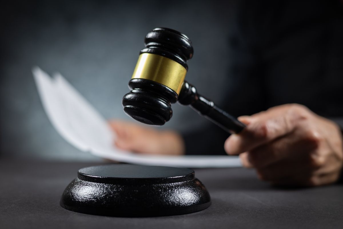 Judge with paper document pronouncing sentence in a court of law. Judge finds the accused guilty, passes judgement and rules case closed. Hand holding gavel and hitting sound block in close-up