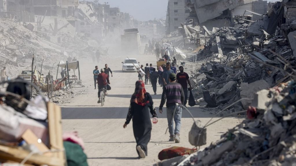 People walk along a heavily damaged street in the northern Gaza Strip on October 16, 2025. Tensions rose after Israel said aid convoys would be reduced due to Hamas slow handover of hostage bodies, even as US officials urged both sides to maintain the ceasefire. (Photo by Abdolrahman Rashad / Middle East Images via AFP)