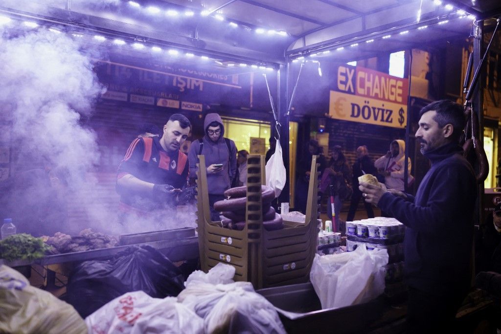 Street vendors sell food at a busy corner in Istanbul as protests carry on nearby, March 25, 2025. Despite a government protest ban, mass demonstrations erupted nationwide following the arrest of Istanbul Mayor Ekrem Imamoglu on corruption charges, with crowds demanding democracy and chanting people, rights, justice. Over one thousand people have been arrested across Turkey, including eight journalists. (Photo by Su Cassiano / Middle East Images via AFP)