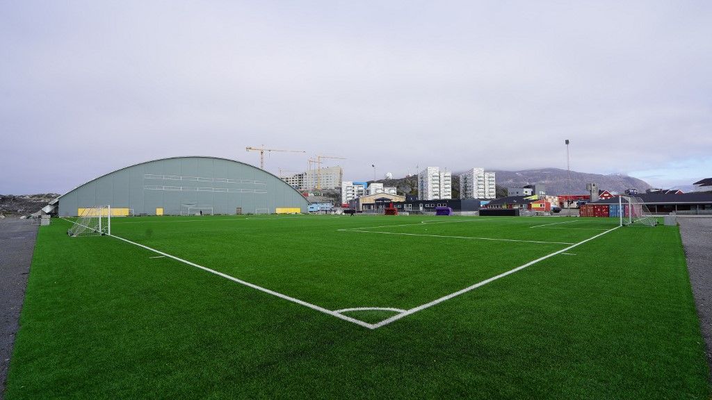 The Nuuk Stadium outdoor artificial pitch is pictured backdropped by buildings and a mountain in Nuuk, Greenland on August 29, 2024. It is a virtually uninhabited territory, covered mainly in ice, and yet, in Greenland, football is king and fans, in search of recognition, want to be able to measure themselves against other nations, a chimera as long as they have not joined a continental federation. (Photo by James BROOKS / AFP) / TO GO WITH AFP STORY by James BROOKS