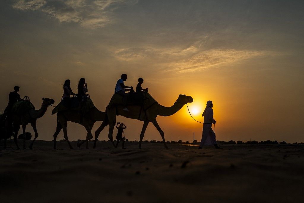 Tourists ride camels at a desert resort in Dubai at sunset on October 19, 2025. (Photo by Jewel SAMAD / AFP)
