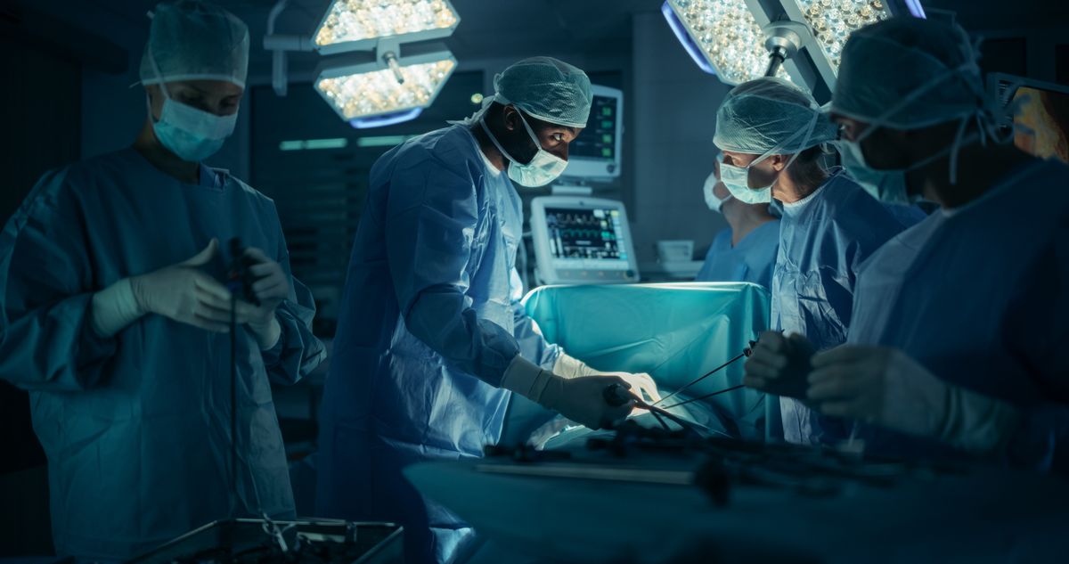 Portrait of a Surgical Team Conducting an Operation in a Dark Hospital Room with Technological Equipment. Black Male Surgeon Having a Discussion with a Nurse while Having an Active Procedure
