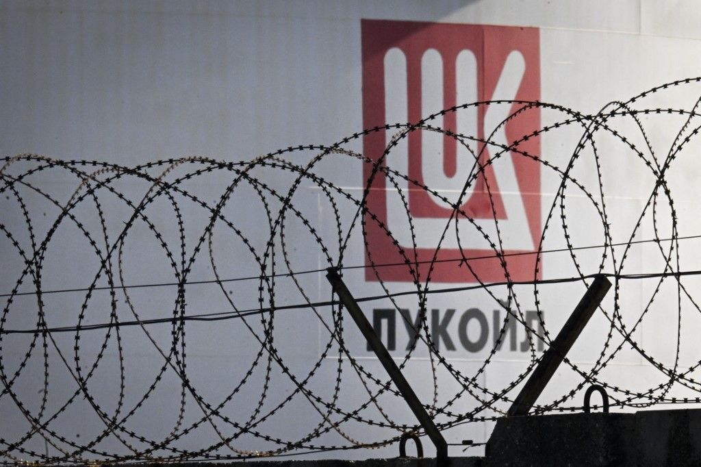This photograph taken on November 14, 2025, shows razor wire in the foreground and the logo of Lukoil on a fuel storage tanks at Rosenets Port terminal near the city of Burgas at the Black sea coast. (Photo by Nikolay DOYCHINOV / AFP)