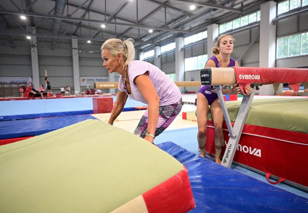 Former Romanian gymnast and actual coach Camelia Voinea (L) arranges a matress for her daughter Sabrina Voinea (R), 17, during a training session at the Dinamo Bucharest training hall in Bucharest July 3, 2024. Long gone are the days when Nadia Comaneci and her compatriots dominated world gymnastics. Today, the Romanian team is a pale shadow, but it wants to believe in its revival for its first participation in the Olympic Games in 12 years. (Photo by Daniel MIHAILESCU / AFP)