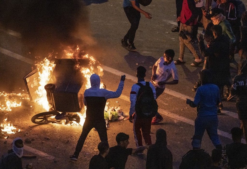 Migrants burn a skip during clashes with Moroccan riot police in the northern town of Fnideq, close to the border between Morocco and Spain's North African enclave of Ceuta on May 19, 2021. Migrants were still trying to cross from Morocco into the Spanish enclave of Ceuta on May 19, 2021, after a record 8,000 people poured over the border this week, escalating tensions between Rabat and Madrid. Some 5,600 migrants had already been sent back, Madrid said, but that did not stop more from trying to make the risky crossing. (Photo by FADEL SENNA / AFP)