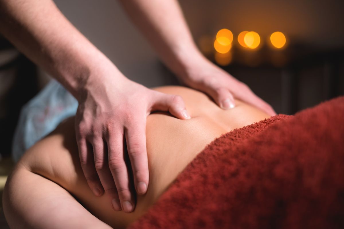 Massage of a female back in a dark room of a spa salon. Male masseur doing massage of the back of the body and lower back