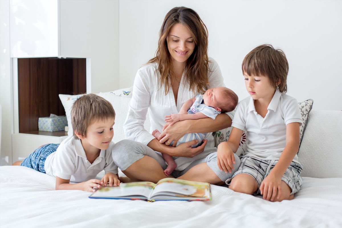 Young mother, read a book to her three children, boys, in the bedroom, mothers day concept