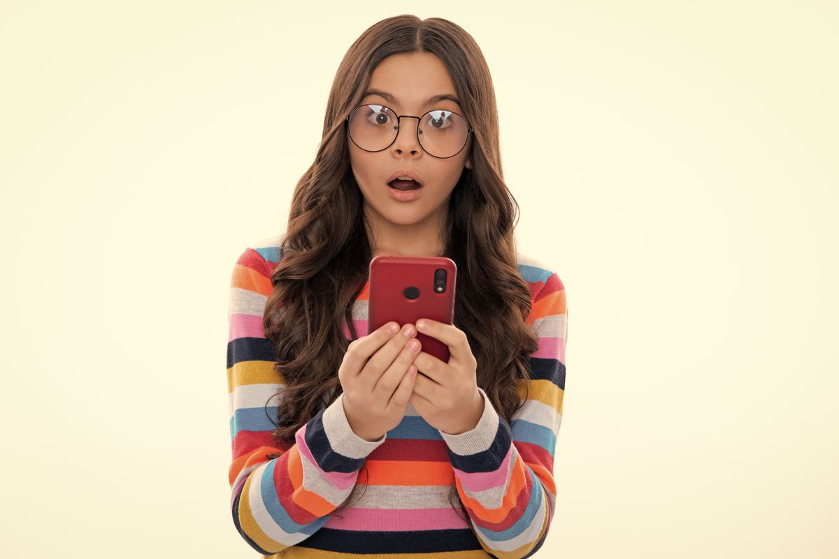 Surprised face, surprise emotions of teenager girl. Close-up portrait of cute teen girl using mobile phone, cell web app, isolated over white background.