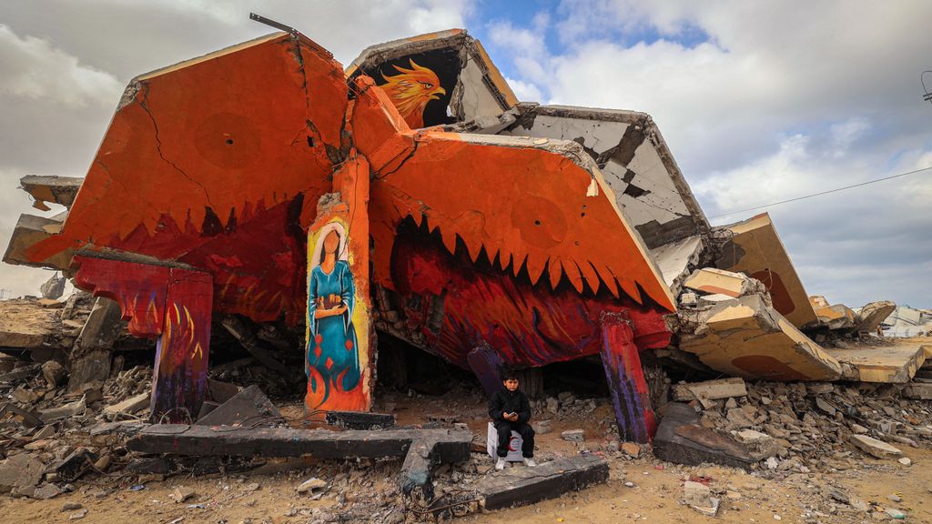 Egy lebombázott épület romjai mellett üldögél egy palesztin fiú a gázai övezetben