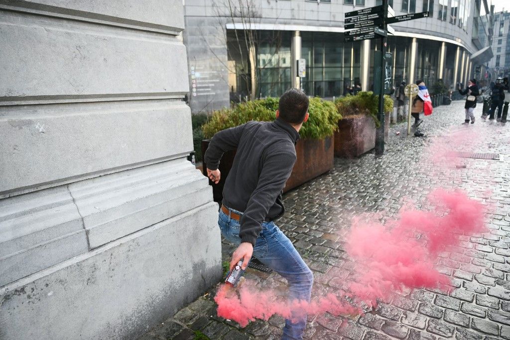 A farmer throws a smoke flare can as farmers clash with police officers near the European Parliament, during a farmers' protest to denounce the reforms of the Common Agricultural Policy (CAP) and trade agreements such as the Mercosur, in Brussels, on December 18, 2025, organised by Copa-Cogeca, the main association representing farmers and agricultural cooperatives in the EU. EU Farmers, particularly in France, worry the Mercosur deal -- which will be discussed at the EU leaders meeting -- will see them undercut by a flow of cheaper goods from agricultural giant Brazil and its neighbours. They also oppose plans put forward by the European Commission to overhaul the 27-nation bloc's huge farming subsidies, fearing less money will flow their way. (Photo by NICOLAS TUCAT / AFP)