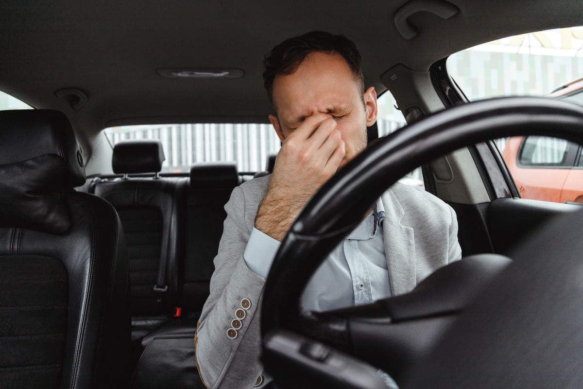 Tired man driver in suit rubbing his eyes behind steering wheel of car.