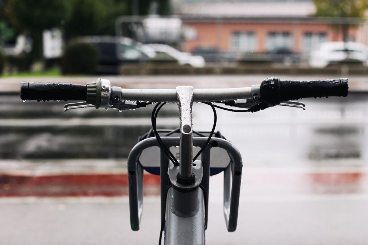 Closeup of bicycle handlebars after rain. Wet metal surface with water drops reflecting urban background. Symbol of mobility, ecology and modern city lifestyle.