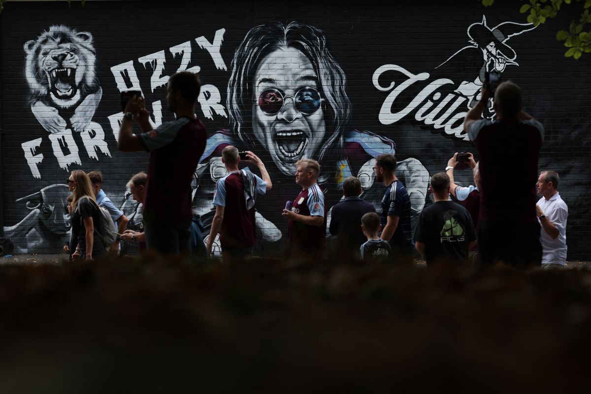 Fans pose beside a new mural of Ozzy Osbourne, commissioned by Aston Villa to remember the singer who died last month, ahead of the English Premier League football match between Aston Villa and Newcastle United at Villa Park in Birmingham, central England on August 16, 2025. (Photo by Adrian Dennis / AFP)
