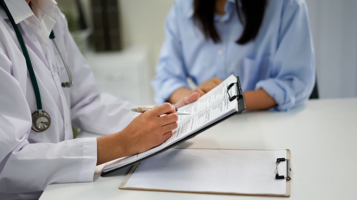 Unknown doctor and patient talking while sitting at the desk in hospital office, close-up of human hands. Medicine and health care concept.