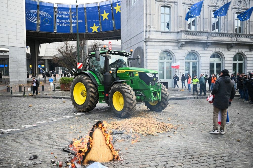Farmers stand next to potatoes and a tractor parked in front of the European Parliament, during a farmers' protest to denounce the reforms of the Common Agricultural Policy (CAP) and trade agreements such as the Mercosur, in Brussels, on December 18, 2025, organised by Copa-Cogeca, the main association representing farmers and agricultural cooperatives in the EU. EU Farmers, particularly in France, worry the Mercosur deal -- which will be discussed at the EU leaders meeting -- will see them undercut by a flow of cheaper goods from agricultural giant Brazil and its neighbours. They also oppose plans put forward by the European Commission to overhaul the 27-nation bloc's huge farming subsidies, fearing less money will flow their way. (Photo by NICOLAS TUCAT / AFP)