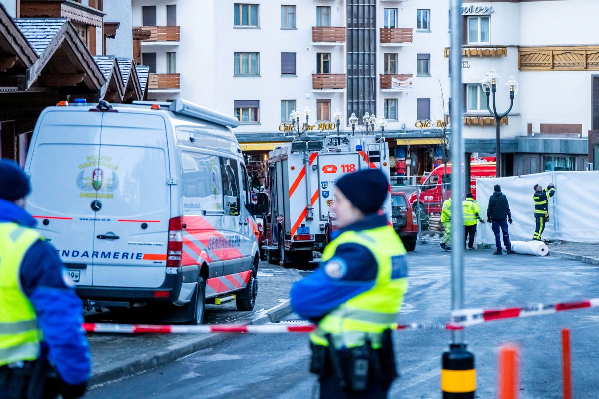 Police officers stand guard at the site of a fire that ripped through the bar Le Constellation  in Crans-Montana on January 1, 2026. Several dozen people are presumed dead and around 100 injured after a fire ripped through a crowded bar in the luxury Swiss ski resort of Crans-Montana, Swiss police said on January 1, 2026. Police, firefighters and rescuers rushed to the popular resort, which is set to host the Ski World Cup from January 30, after the fire broke out in the early hours of New Year's Day. (Photo by MAXIME SCHMID / AFP)