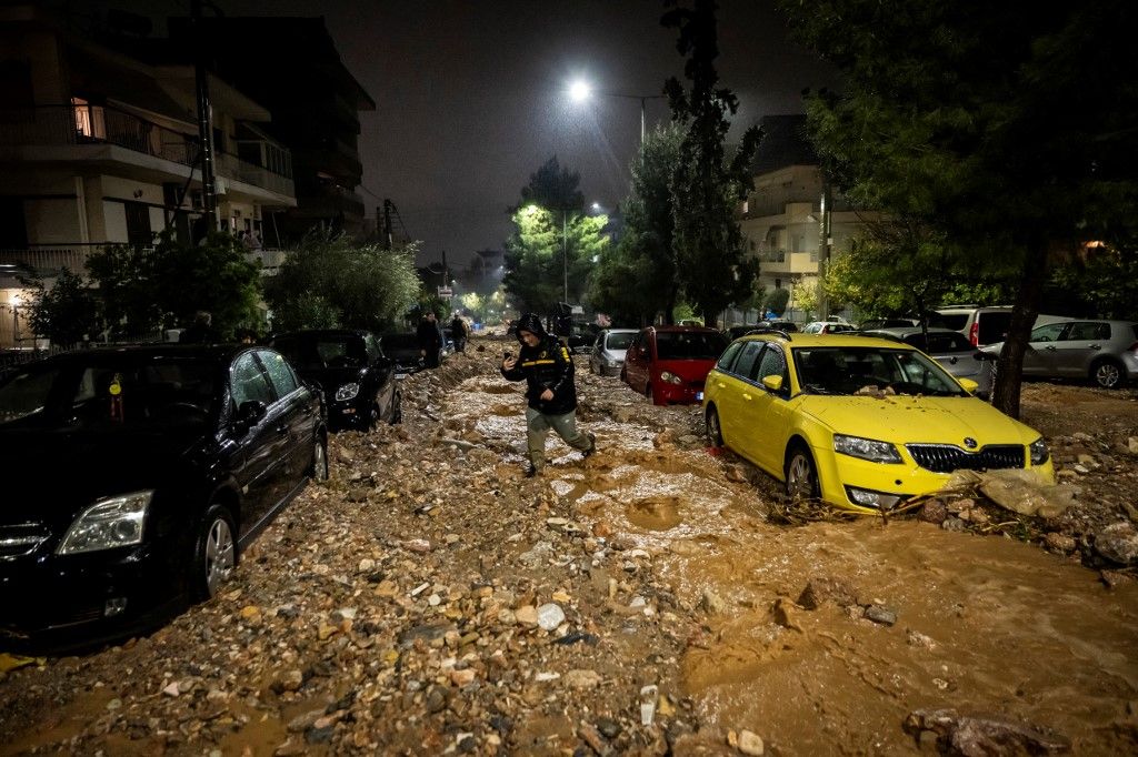 A man crosses a flooded street covered with rubbles after a heavy rainfalls in Ano Glyfada, southern of Athens, on January 21, 2026. (Photo by Aris MESSINIS / AFP)