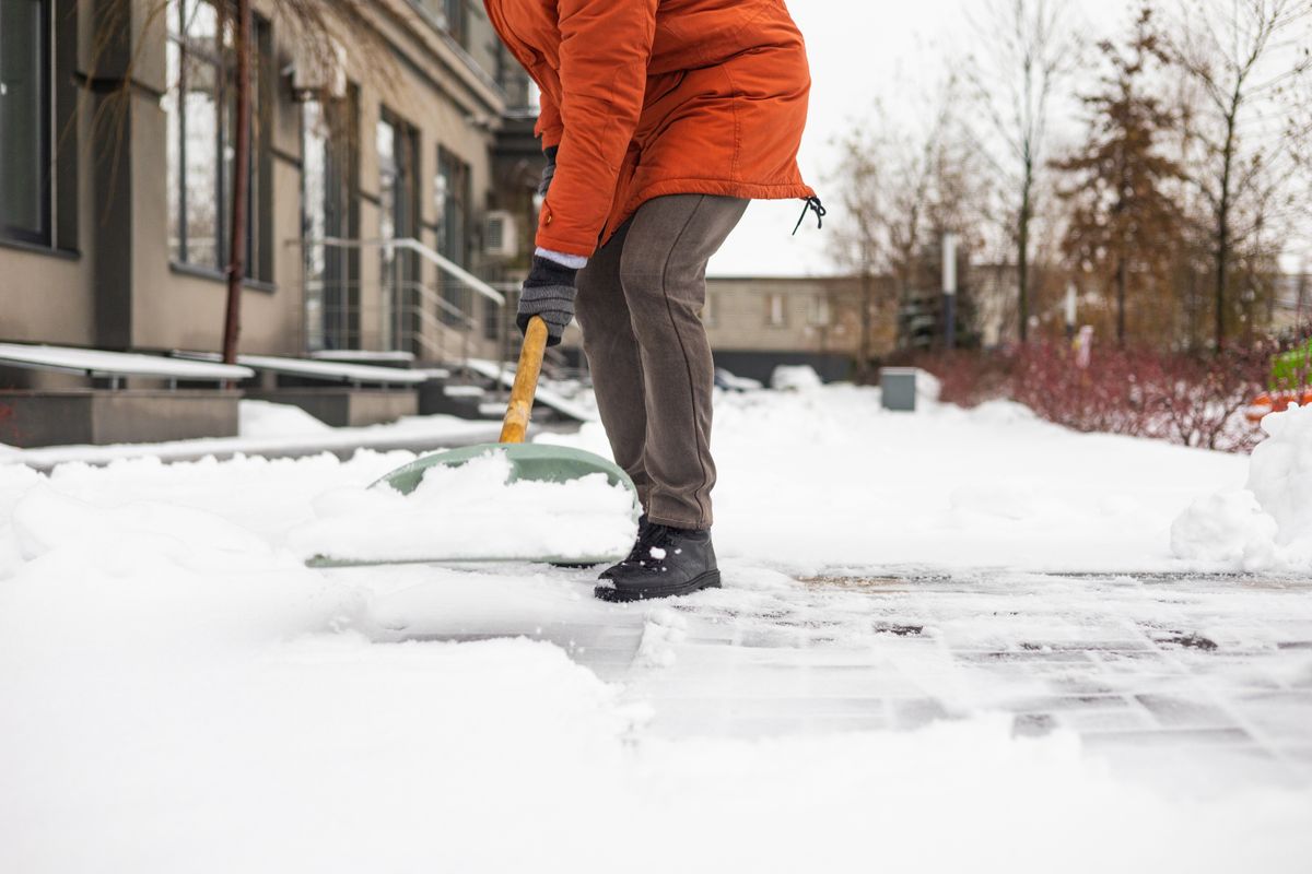 Close-up of a man cleaning and clearing snow in front of the house on a sunny and frosty day. Cleaning the street from snow on a winter day. Snowfall, and a severe snowstorm in winter.