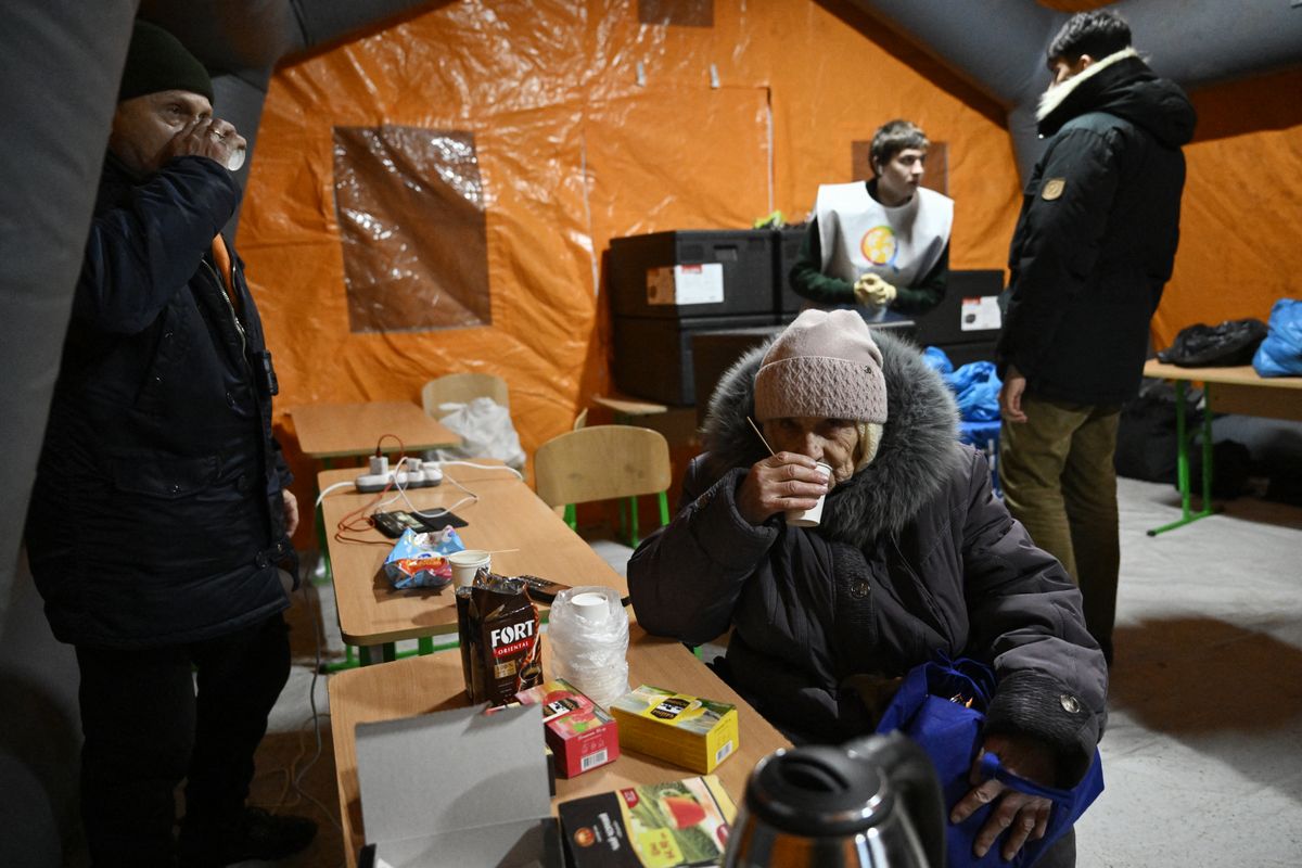 People warm themselves in an emergency service tent set up for those whose homes are without electricity or heating following Russian missile and drone attacks on Ukrainian energy infrastructure, in a residential neighborhood of Kyiv on January 22, 2026  amid the Russian invasion in Ukraine. (Photo by Genya SAVILOV / AFP)