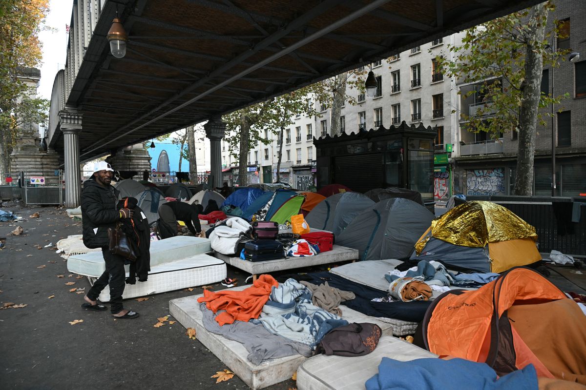A migrant walks by a makeshift camp set up under the overhead railway line at Stalingrad metro station as police prepare to clear away the encampment in Paris early on November 5, 2025. (Photo by Bertrand GUAY / AFP)