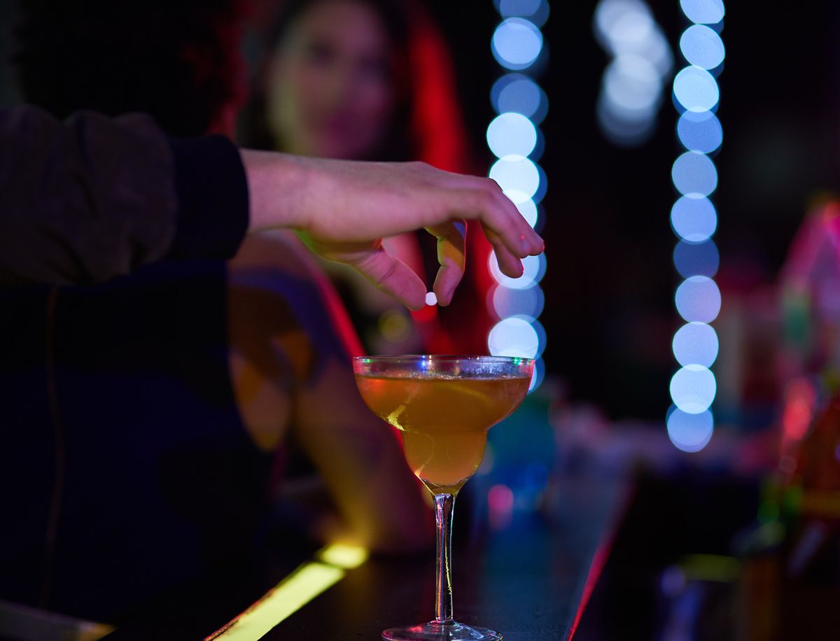 Closeup shot of a man dropping a pill into a woman's cocktail in a nightclub