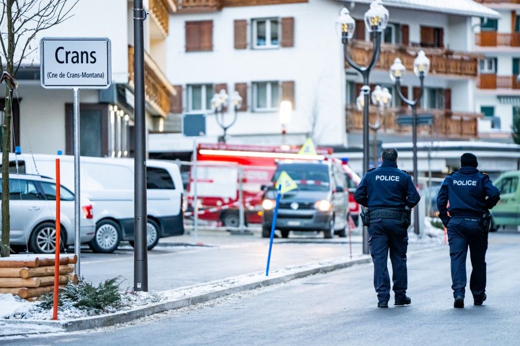 Police officers walk near ambulances at the site of a fire that ripped through the bar Le Constellation in Crans-Montana on January 1, 2026. Several people were killed and others injured when an explosion ripped through a bar in the luxury Alpine ski resort town of Crans Montana, Swiss police said early on January 1. (Photo by MAXIME SCHMID / AFP)