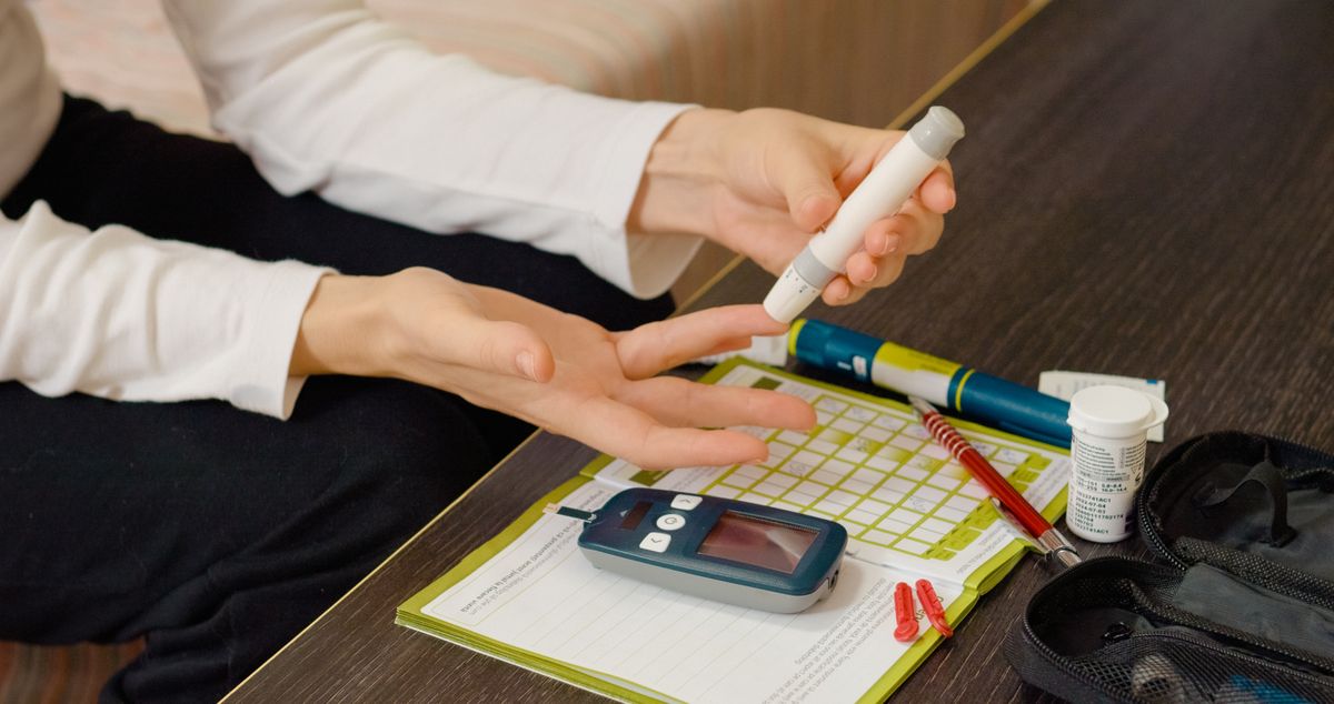 A woman carefully pricks her finger with a pen to check her blood sugar level using a glucometer. She monitors her health while managing diabetes at home.