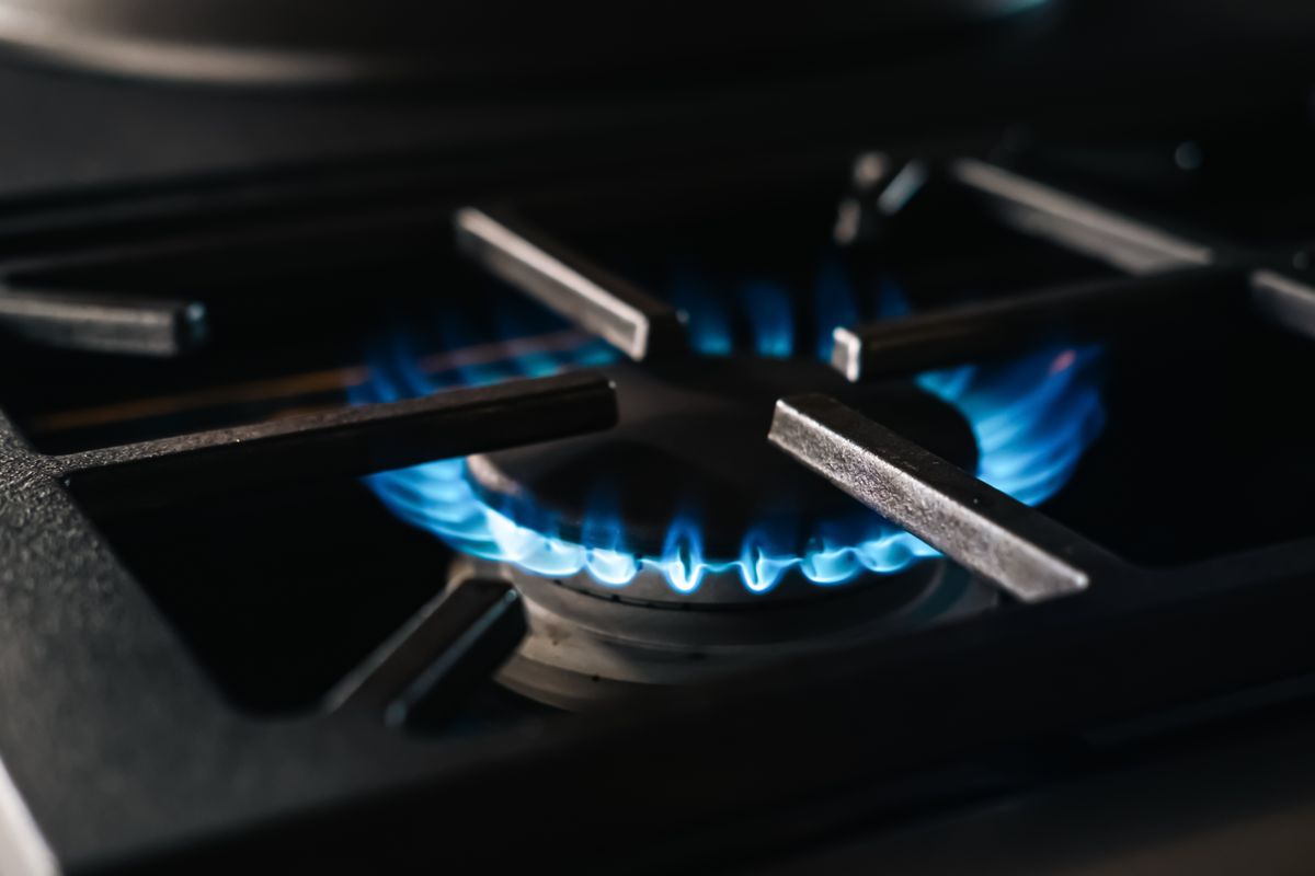 Close-up of a gas stove burner with blue flames glowing, symbolizing energy and cooking potential. The warm ambiance showcases domestic detail, comfort, and functionality.