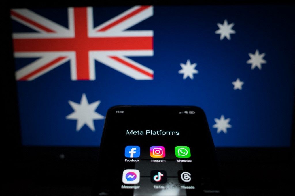 Social network logos display on a smartphone screen and the Australian flag appears on a computer screen in this photo illustration in Athens, Greece, on November 21, 2024. The Australian government proposes a ban on social media for all citizens under 16. Citing the success of recently introduced restrictions on mobile phones in Australian schools, the prime minister announces the ban by declaring that it is doing harm to children and he is calling time on it. (Photo by Nikolas Kokovlis/NurPhoto) (Photo by Nikolas Kokovlis / NurPhoto via AFP)