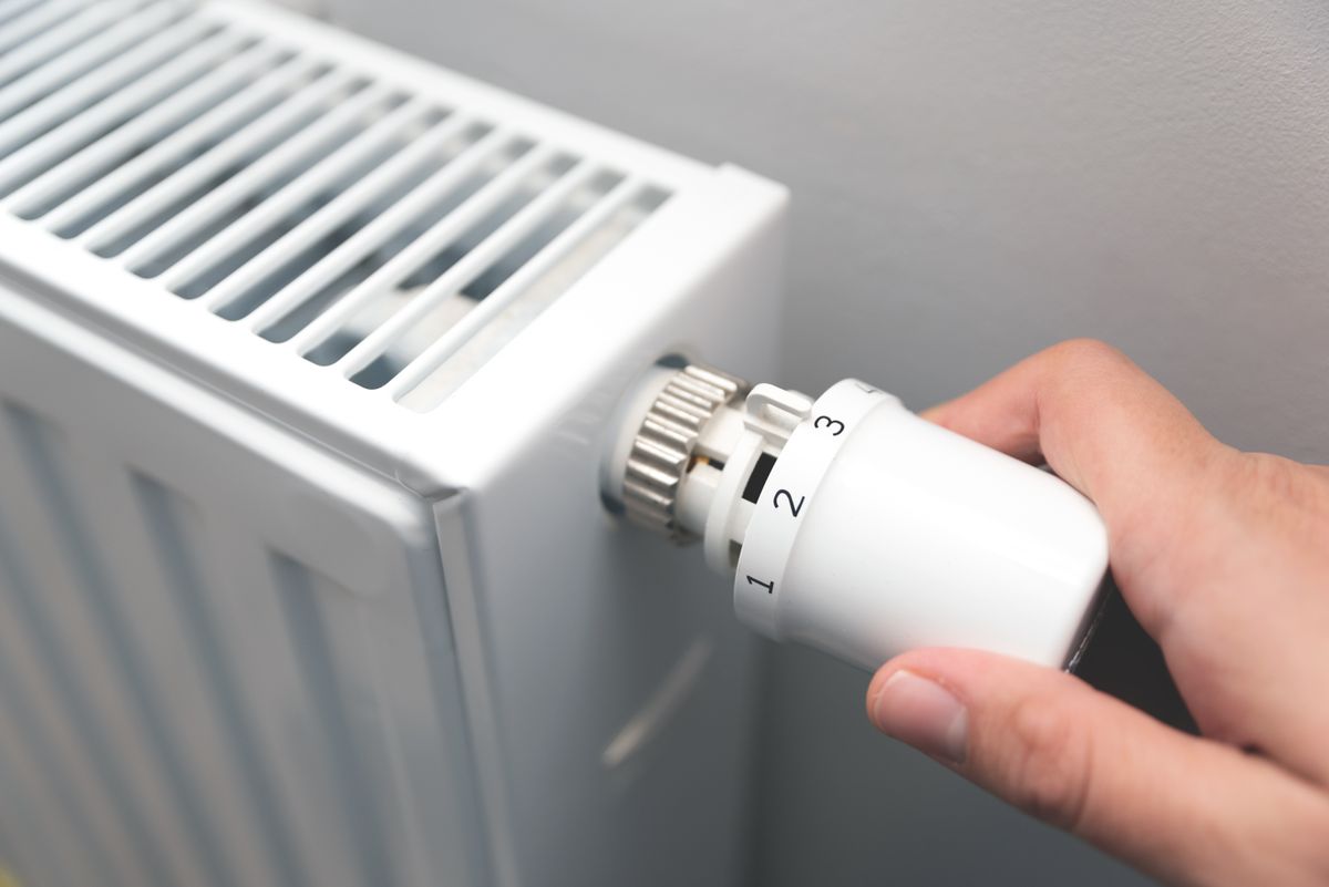 Person is adjusting the temperature on a radiator. The radiator is white and has a knob on it