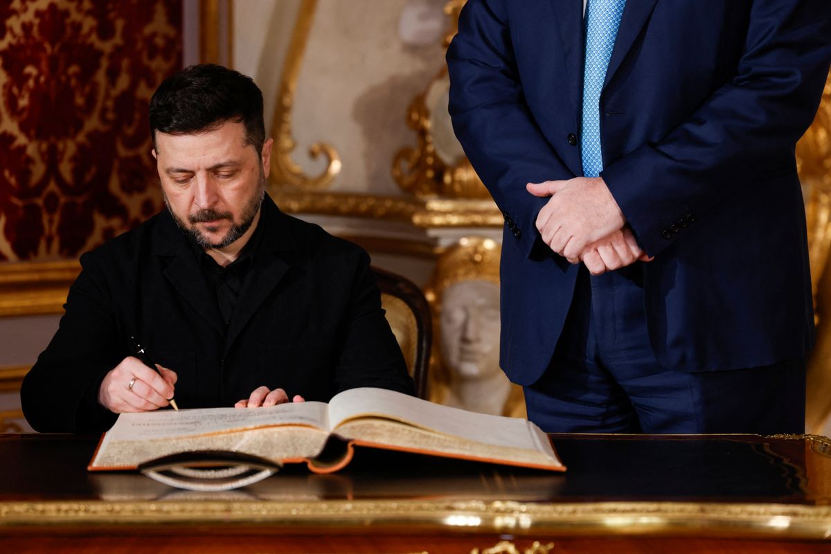 Bavarian State Premier Markus Soeder (R) looks on as Ukrainian President Volodymyr Zelensky signs the guest book at the Munich Residence palace, prior to the traditional dinner on the occasion of the Munich Security Conference (MSC), on February 14, 2026 in Munich, southern Germany. (Photo by Michaela STACHE / AFP) Zelenszkij