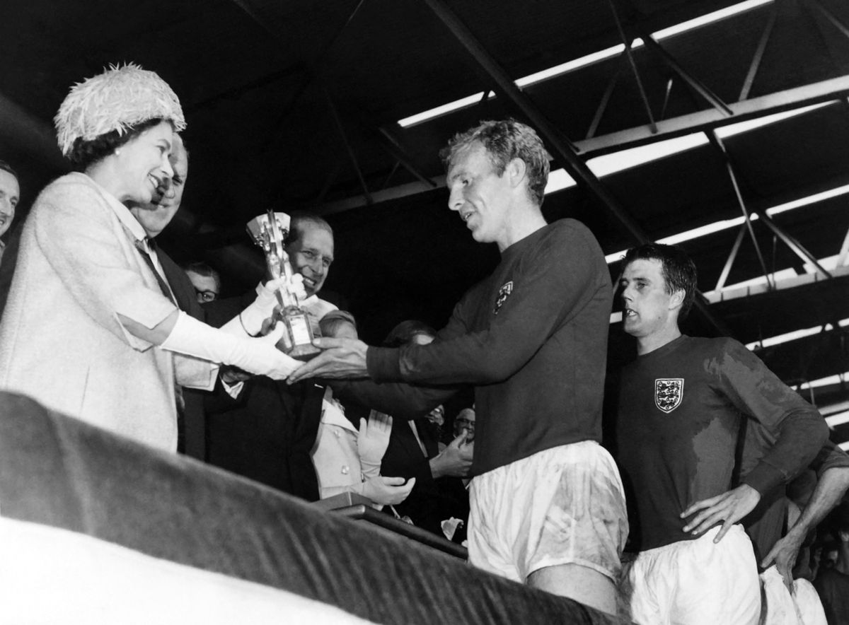 Britain's Queen Elizabeth of England presents the Jules Rimet Cup to Bobby Moore, captain of England's national soccer team, as her husband Prince Philip (C) and forward Geoff Hurst (R) look on after England beat West Germany 4-2 in extra time in the World Cup final 30 July 1966 at Wembley stadium in London. Hurst scored three goals, two of them in extra time, to help England win its first World title. (Photo by AFP)