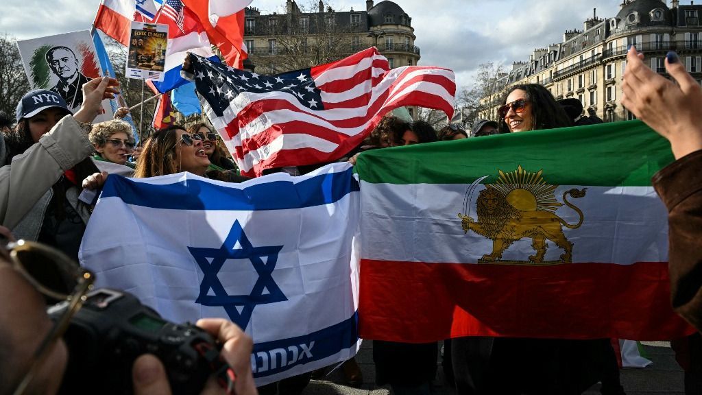 Anti-Iranian regime protesters wave a giant Iranian flag before the 1979 revolution with the Lion and Sun emblems (R), an Israeli flag (L) and a US flag (rear C) as they gather during a march in support of the US and Israel attack on Iran and the killing of Iran's supreme leader, in Paris on March 1, 2026. Iranian state television confirmed the death of Iran's supreme leader Ayatollah Ali Khamenei on February 28, 2026, after US President said he had been killed. The announcement came after the United States and Israel started launching waves of strikes against targets in Iran, sparking swift retaliation by the Islamic republic. (Photo by Anna KURTH / AFP)