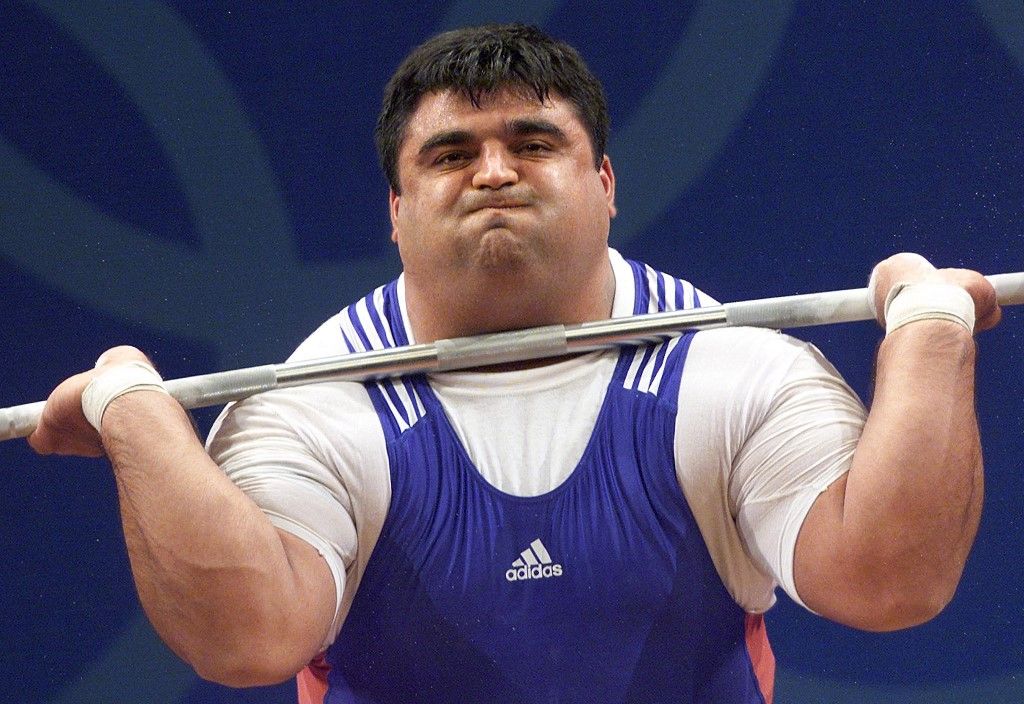 Hossein Rezazadeh of Iran grimaces as he lifts his way to an Olympic gold medal and new Olympic and World records in the Men's 105Kg  group B, 26 September at the Sydney 2000 Olympic Games. Rezazadeh broke the snatch world record with 212.5 Kg from 206 Kg and the combined total world record of 472.5 Kg from 465 Kg with a clean and jerk of 260.0 Kg ahead of Germany' Ronny Weller who took silver while also breaking world records in the snatch and the combined total before to be topped by Rezazadeh. AFP PHOTO/EMMANUEL DUNAND (Photo by EMMANUEL DUNAND / AFP)