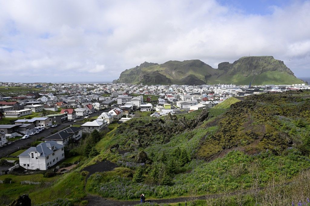 A photo taken on June 26, 2023 shows a view over the town of Vestmannaeyjabær on Heimaey on the Icelandic archipelago of Vestmannaeyjar, Westman Islands, while in the foreground hardened lava from the volcanic eruption in 1973 is seen. (Photo by Halldor KOLBEINS / AFP)