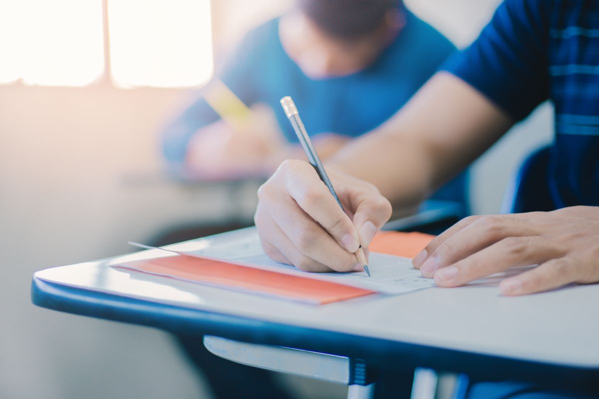 soft focus.high school or university student holding pencil writing on paper answer sheet.sitting on lecture chair taking final exam attending in examination room or classroom.student in uniform