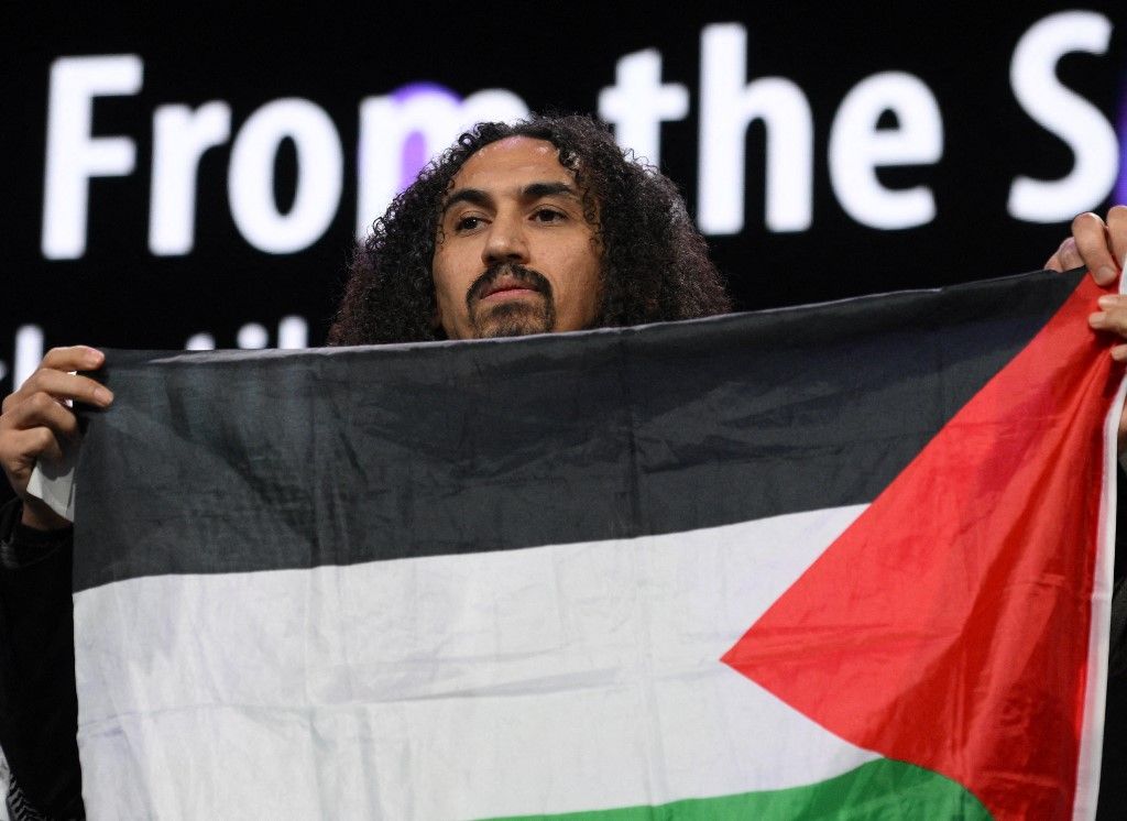 Syrian-Palestinian director Abdallah Alkhatib stands on stage with a Palestinian flag as he accepts the GWFF Best Feature Film Debut Award for Chronicles From the Siege during the Award Ceremony of the 76th Berlinale, Europe's first major film festival of the year, in Berlin on February 21, 2026. German culture officials plan to summon on February 26, 2026 organisers of the Berlin film festival after the event was rocked this year by controversy over the Israel-Palestinian conflict and Gaza war. The Culture minister's office confirmed to AFP that an extraordinary supervisory board meeting of the KBB will be held on February 26, 2026 to discuss "the direction of the Berlinale", but said it would "not comment on further speculation". (Photo by RALF HIRSCHBERGER / AFP)