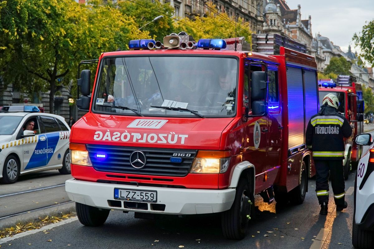 Budapest, Hungary - Oct 23, 2025: Hungarian firefighters respond to an emergency in the city center. A red fire truck with flashing lights and officers in uniform stand on a busy urban street.