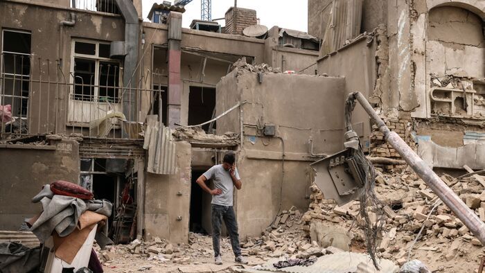 Lebombázott házak előtt telefonál egy férfi az iráni fővárosban, Teheránban