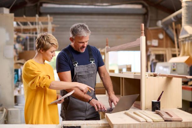 Female Apprentice Learning Skills From Mature Male Carpenter In Furniture Workshop, kkv