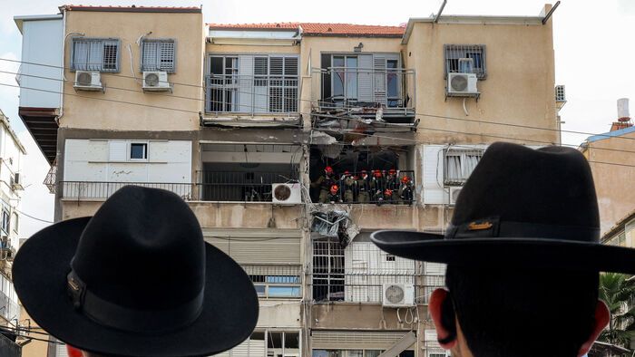 Ultraortodox zsidó férfiak figyelik, ahogy az izraeli biztonsági erők vizsgálnak egy iráni lövedék által eltalált épületet 