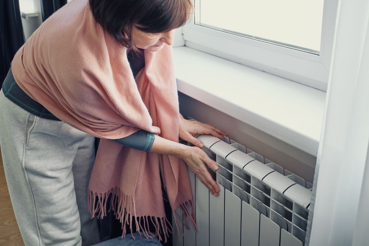Woman touching cold radiator worrying about rising energy costs at home